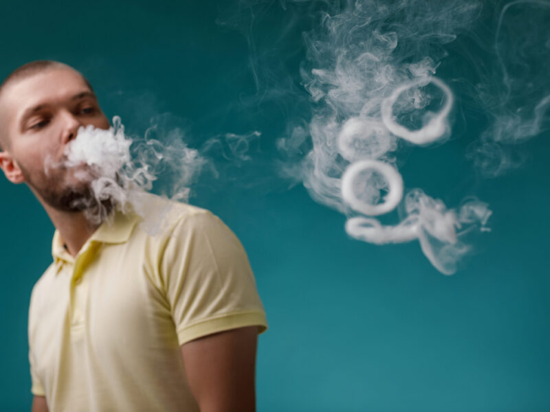 vaping man smoking e-cigarette. Guy launches ring of white smoke. focus on smoke