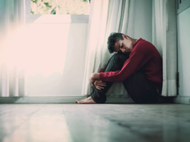 man hugging his knees while sitting in a corner