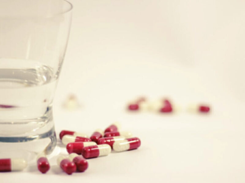 red and white pills spilled out next to a glass of water