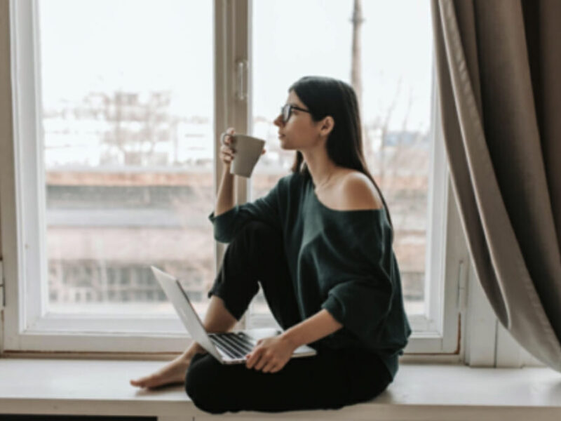 woman sitting on window ledge drinking coffee