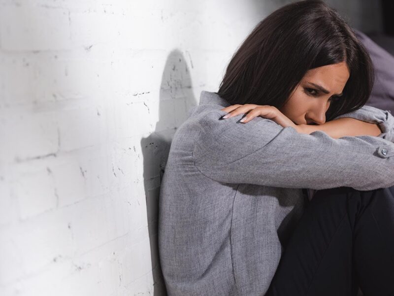 upset woman sitting against a wall with arms crossed