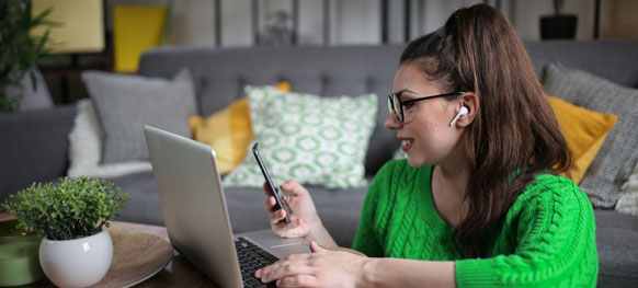 A woman in a green sweater sits on a couch, focused on her laptop, creating a cozy and productive atmosphere.