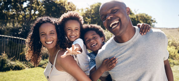 A joyful family smiles together while sitting on the grass, enjoying a sunny day outdoors.