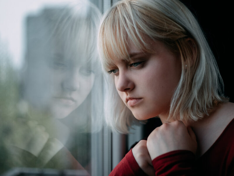 A melancholy blonde woman leaning her head against a window