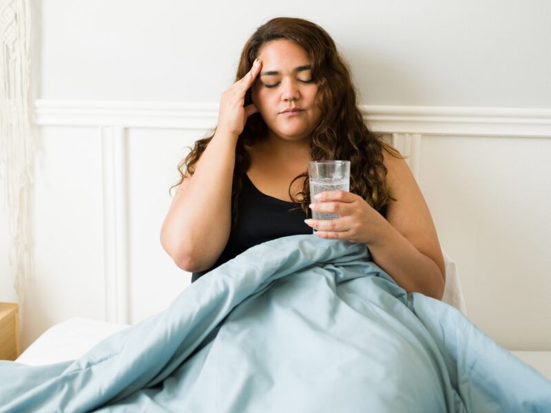 A women sitting upright in bed, holding a glass of water, nursing a hangover