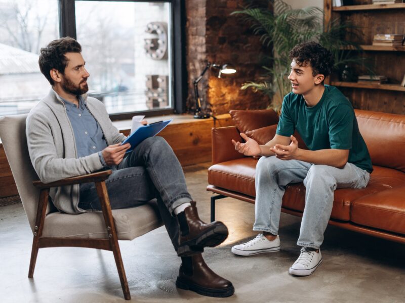 A male teenager speaking to his therapist while sitting on a couch.