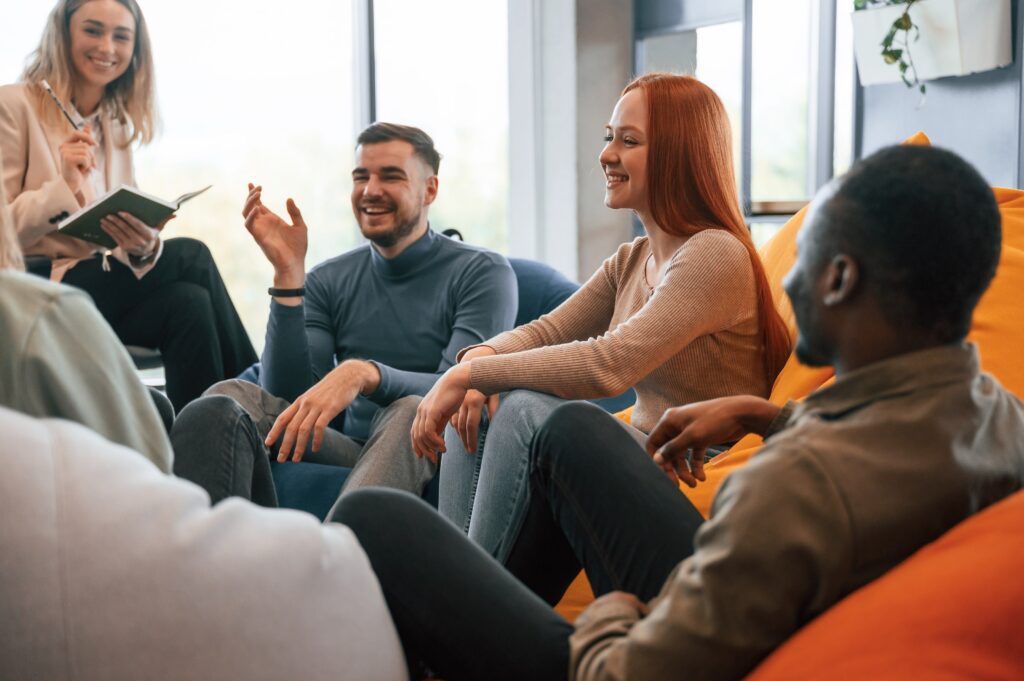 A group of cheerful young adults going through group therapy in a brightly lit room.