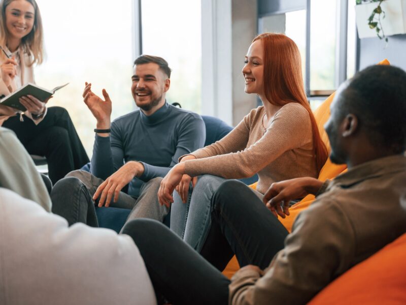 A group of cheerful young adults going through group therapy in a brightly lit room.